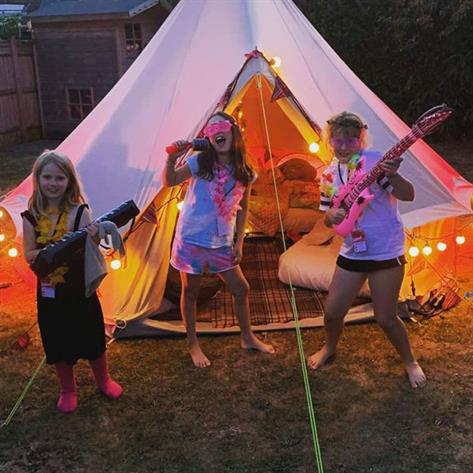 Three children with guitars outside a bell tent